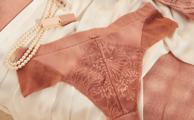 Bruine kanten slip op een witte doek, naast een parelketting en een lipstick